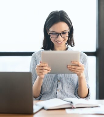 Young girl holding tablet and using laptop at office